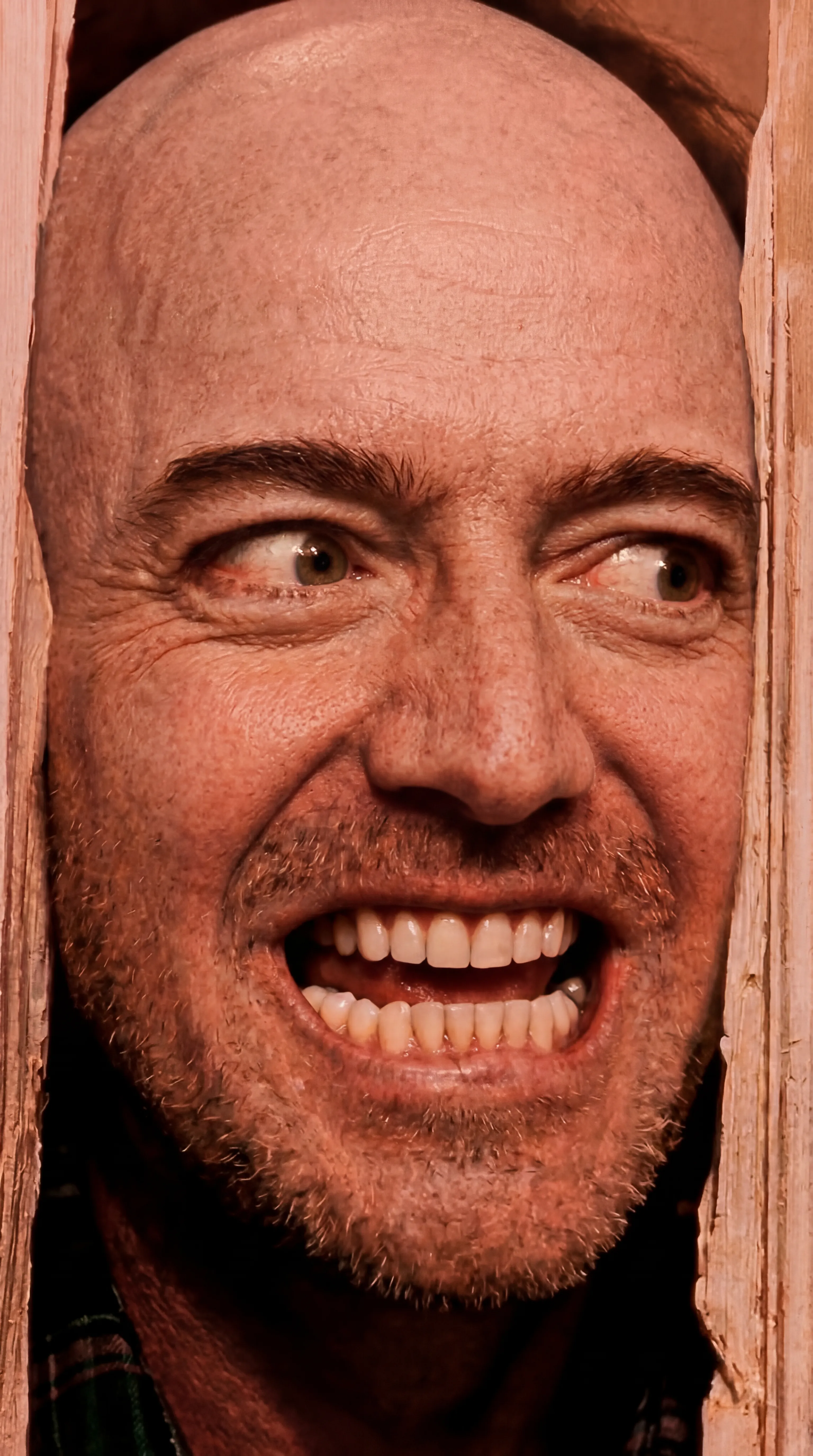 Man grinning through a cracked wooden door in warm sepia tones